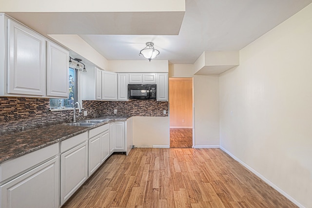 kitchen featuring light wood-type flooring, tasteful backsplash, dark stone counters, sink, and white cabinetry