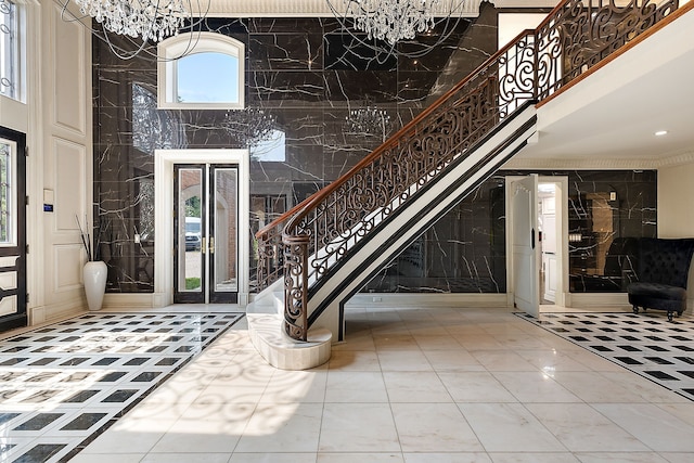 tiled foyer featuring french doors, a towering ceiling, a chandelier, and tile walls