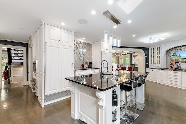 kitchen with pendant lighting, a large island with sink, white cabinets, decorative backsplash, and a breakfast bar area