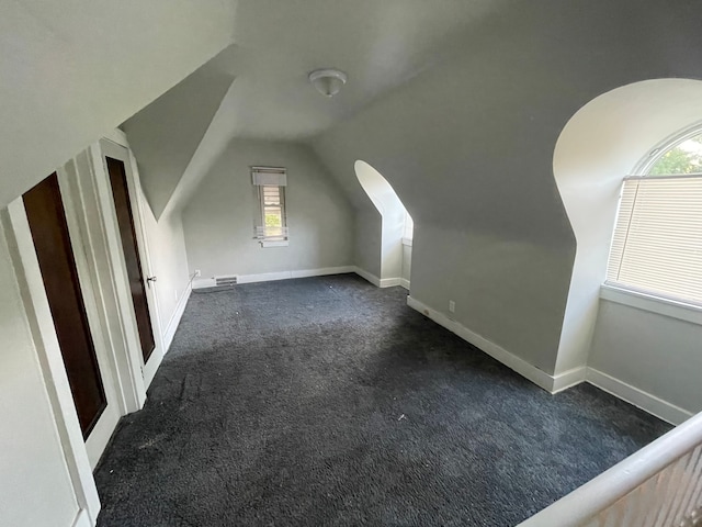 additional living space featuring dark colored carpet, plenty of natural light, and lofted ceiling