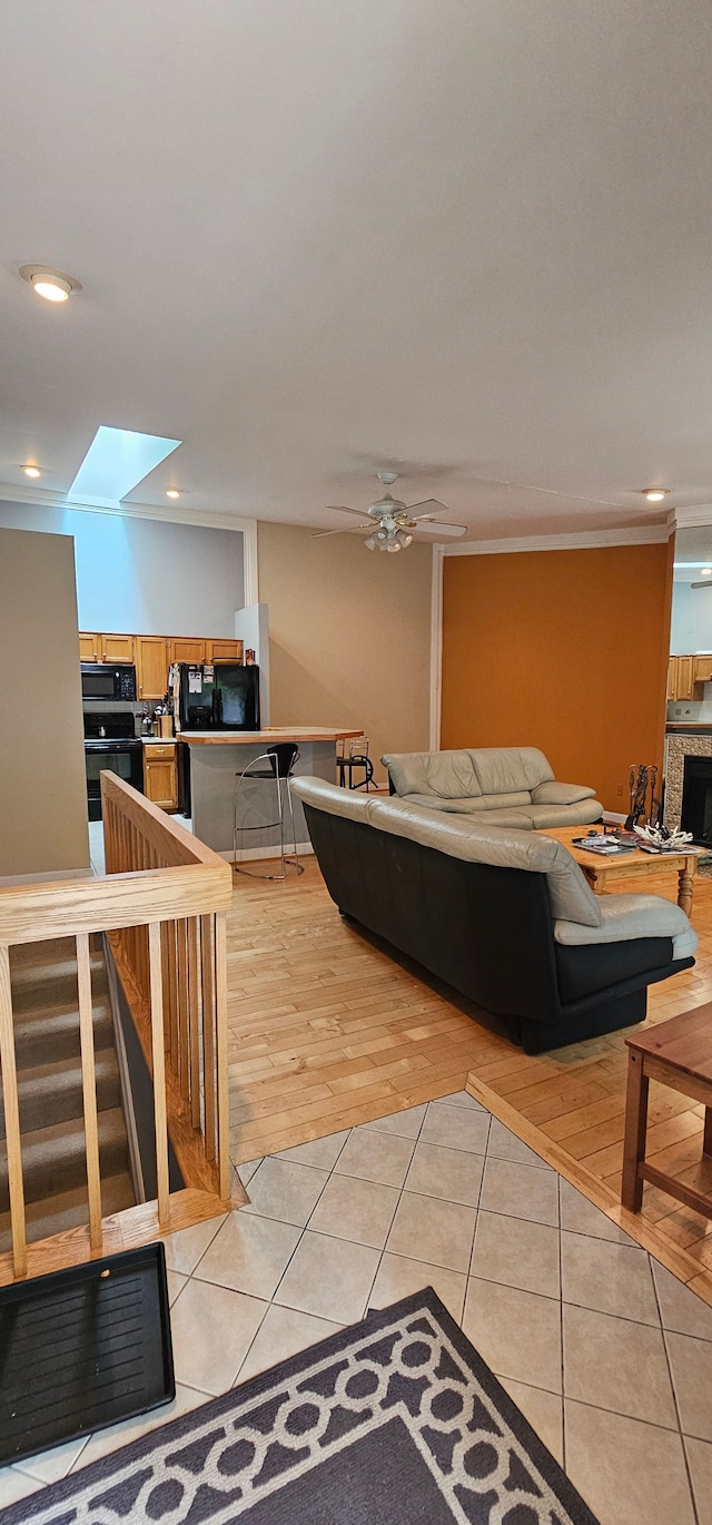 tiled living room featuring a skylight, ceiling fan, and crown molding