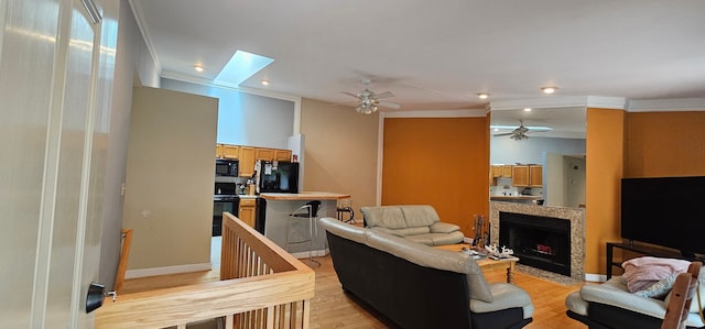 living room featuring a skylight, light hardwood / wood-style flooring, ceiling fan, and ornamental molding