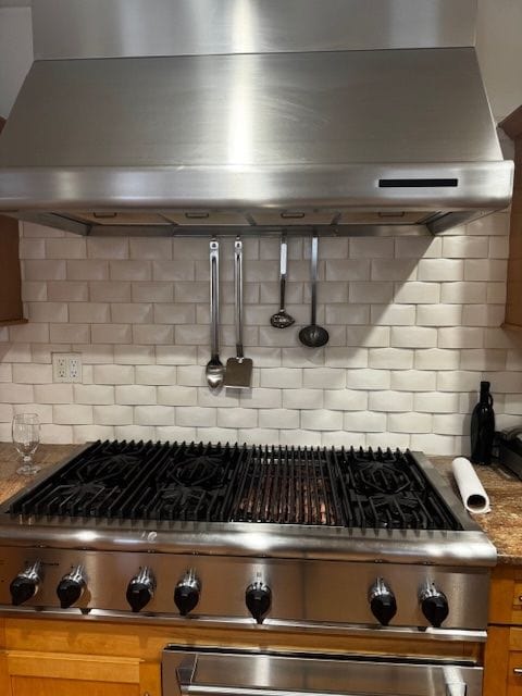 interior details featuring wall chimney exhaust hood, tasteful backsplash, and stone counters