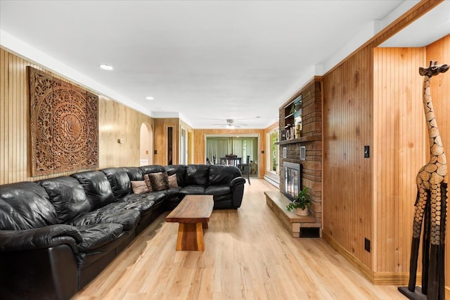 living room featuring a fireplace, wooden walls, light hardwood / wood-style flooring, and ceiling fan