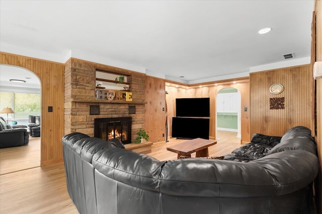 living room with a stone fireplace, wooden walls, and light hardwood / wood-style flooring