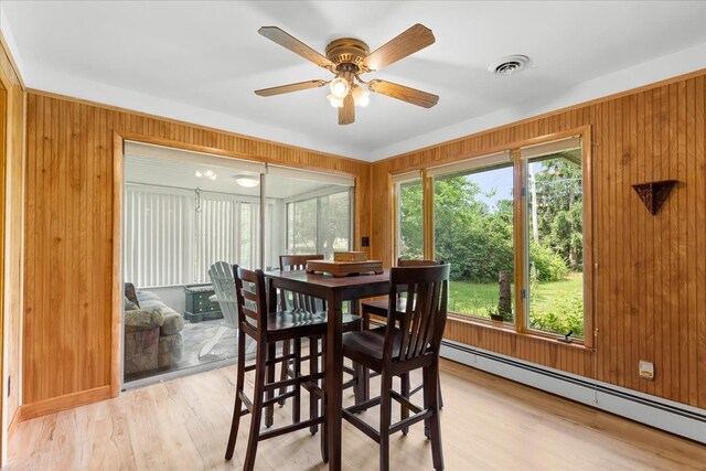 dining area featuring light wood-type flooring, ceiling fan, a baseboard heating unit, and wood walls