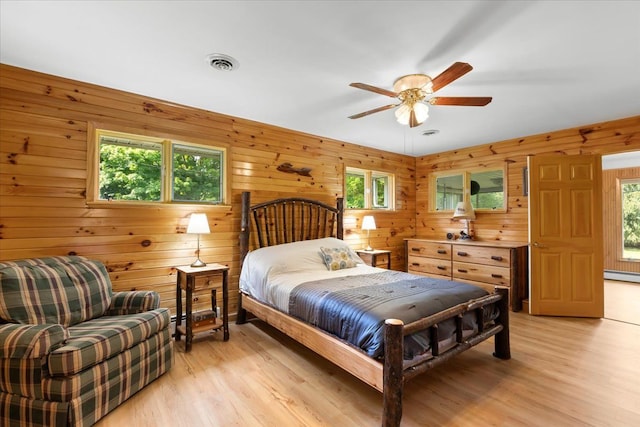 bedroom featuring multiple windows, wooden walls, ceiling fan, and light wood-type flooring