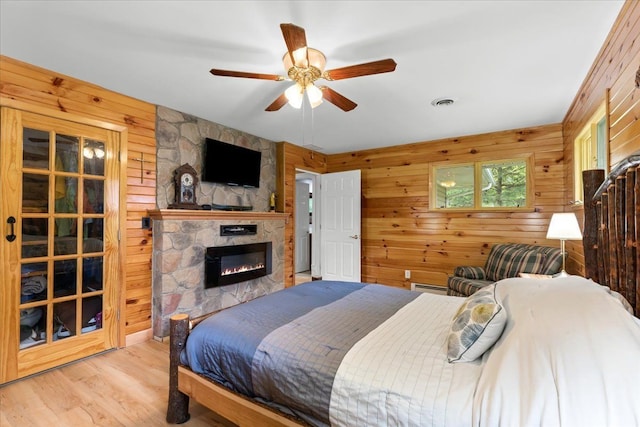 bedroom with a fireplace, wood walls, ceiling fan, baseboard heating, and light hardwood / wood-style flooring