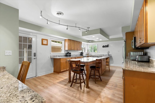 kitchen with a kitchen bar, a center island, light hardwood / wood-style flooring, and light stone countertops