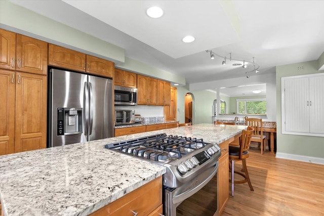 kitchen with light stone countertops, a kitchen breakfast bar, stainless steel appliances, light hardwood / wood-style flooring, and a kitchen island