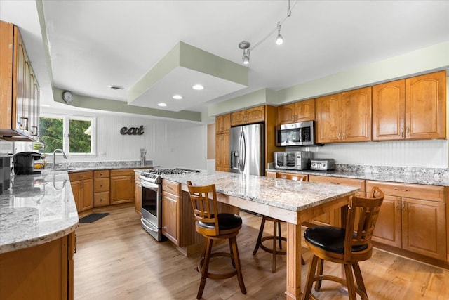 kitchen featuring light stone countertops, stainless steel appliances, a kitchen island, and light hardwood / wood-style floors