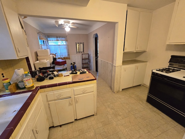 kitchen featuring gas stove, ceiling fan, sink, tile countertops, and white cabinets