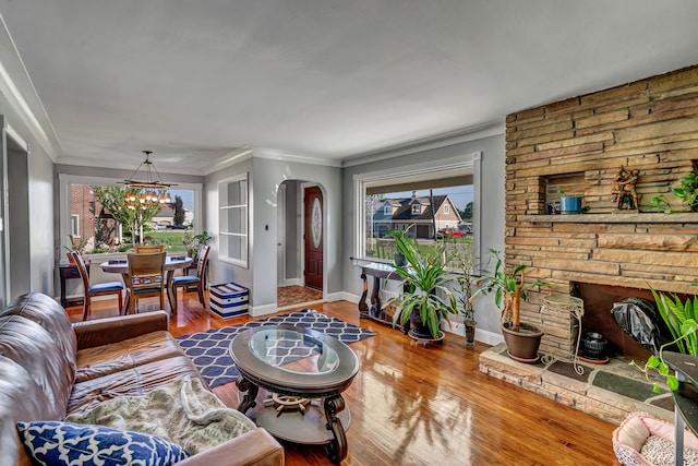 living room with hardwood / wood-style floors, an inviting chandelier, ornamental molding, and a stone fireplace