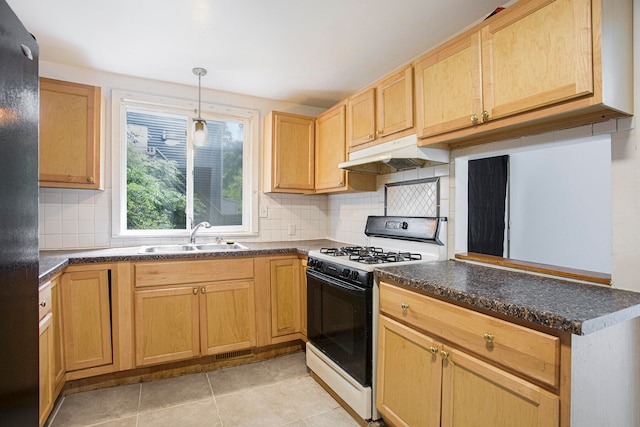 kitchen with under cabinet range hood, range with gas cooktop, dark countertops, and a sink