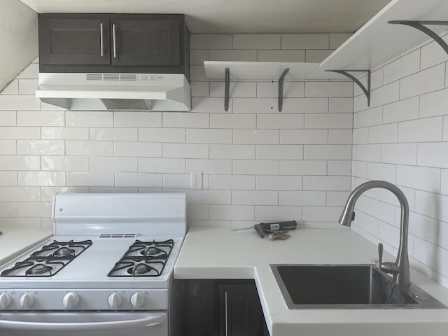 kitchen featuring under cabinet range hood, a sink, gas range gas stove, tasteful backsplash, and light countertops