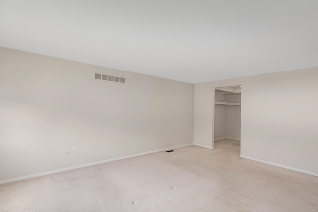 unfurnished bedroom featuring a walk in closet, a closet, and light colored carpet