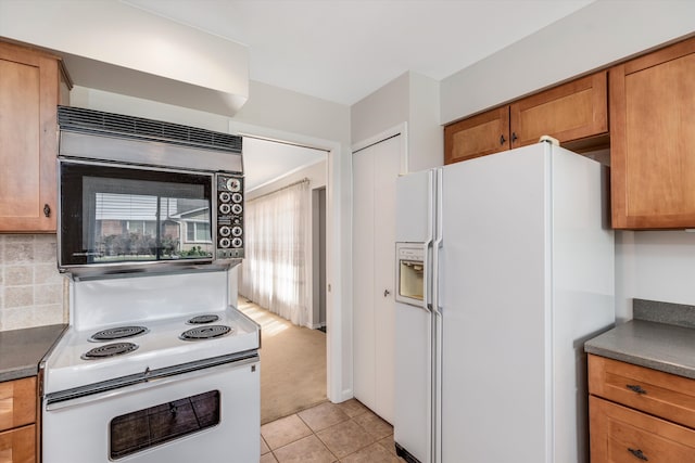 kitchen featuring backsplash, light tile patterned floors, and white appliances