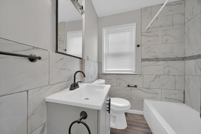 full bathroom with vanity, tile walls, hardwood / wood-style floors, toilet, and tiled shower / bath