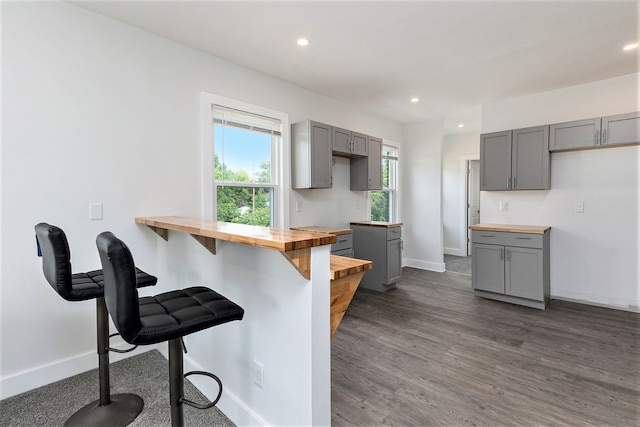 kitchen featuring gray cabinets, dark hardwood / wood-style flooring, butcher block counters, and a breakfast bar area