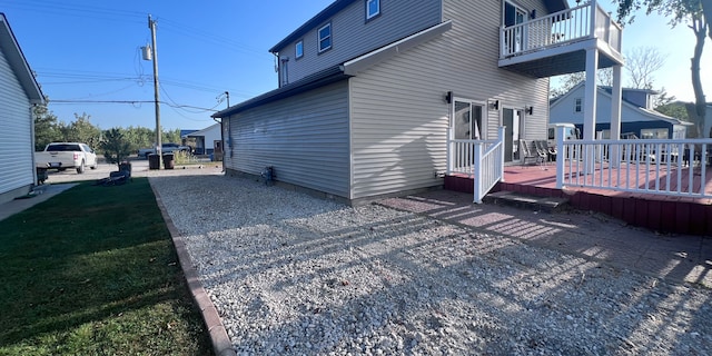 view of side of home featuring a lawn, a balcony, and a wooden deck