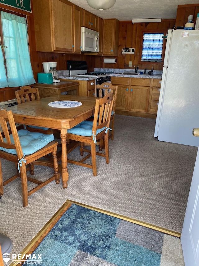 kitchen with carpet, white appliances, a textured ceiling, and wooden walls