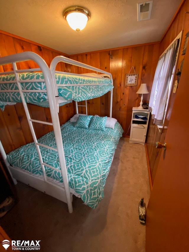 bedroom with wood walls, light colored carpet, and a textured ceiling