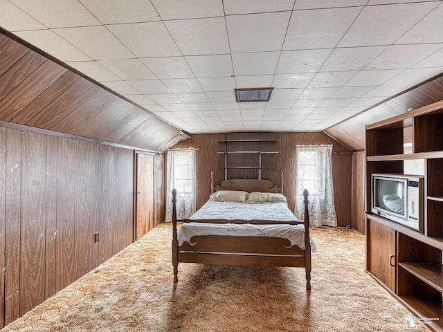 carpeted bedroom featuring vaulted ceiling, wooden walls, and multiple windows