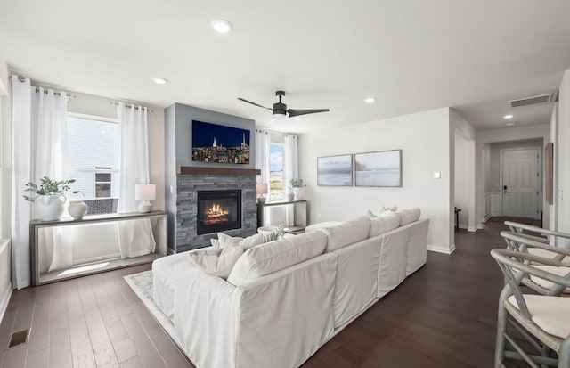 living room with dark hardwood / wood-style floors, ceiling fan, and a stone fireplace