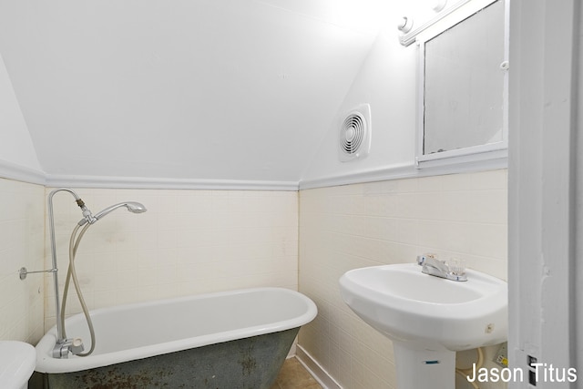 bathroom with tile patterned flooring, a bath, lofted ceiling, and tile walls