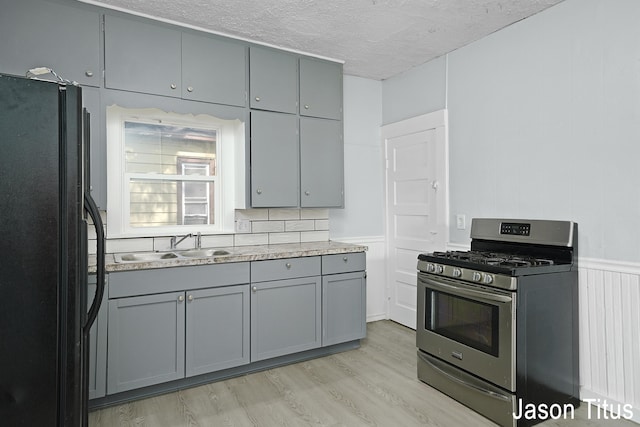 kitchen featuring black fridge, stainless steel range with gas cooktop, gray cabinets, and light wood-type flooring