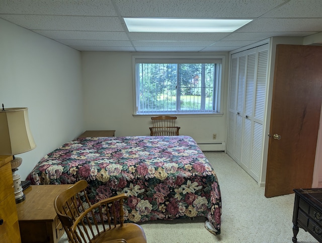 bedroom with a paneled ceiling, a closet, light colored carpet, and a baseboard heating unit