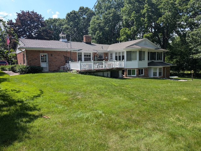 rear view of property featuring a sunroom, a wooden deck, and a lawn