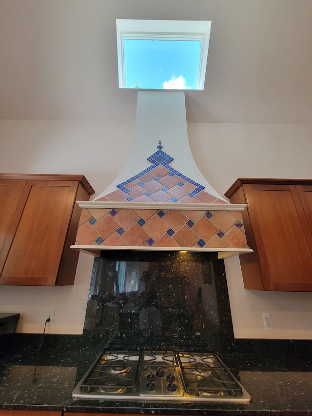 kitchen with stainless steel gas stovetop, dark stone countertops, and wall chimney range hood