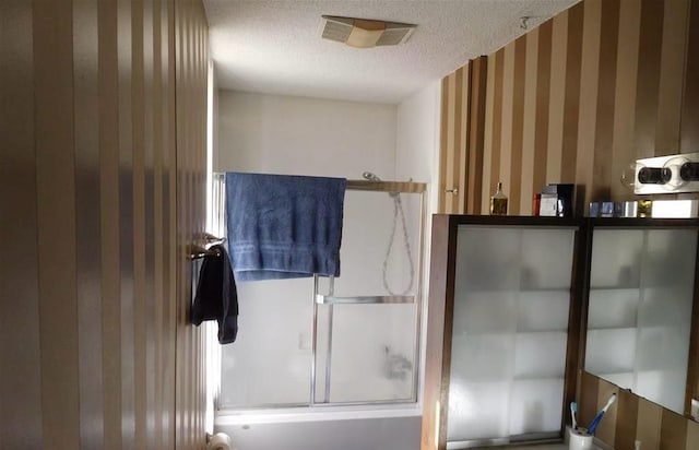 bathroom featuring combined bath / shower with glass door and a textured ceiling