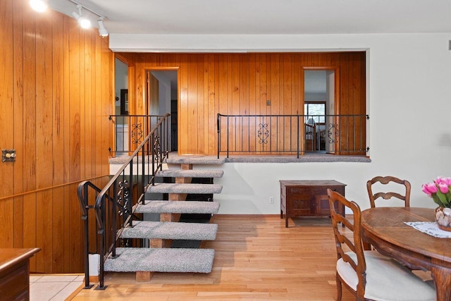 stairs featuring hardwood / wood-style floors, wooden walls, and track lighting