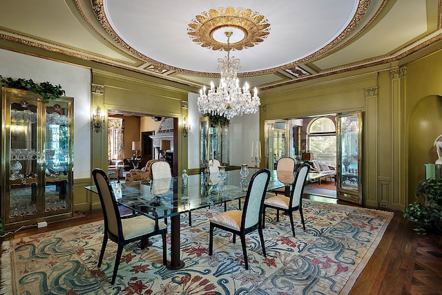 dining space featuring a raised ceiling, dark wood-type flooring, ornamental molding, and an inviting chandelier