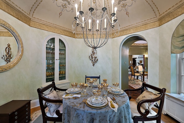 dining room featuring a chandelier, wood-type flooring, radiator heating unit, and a high ceiling