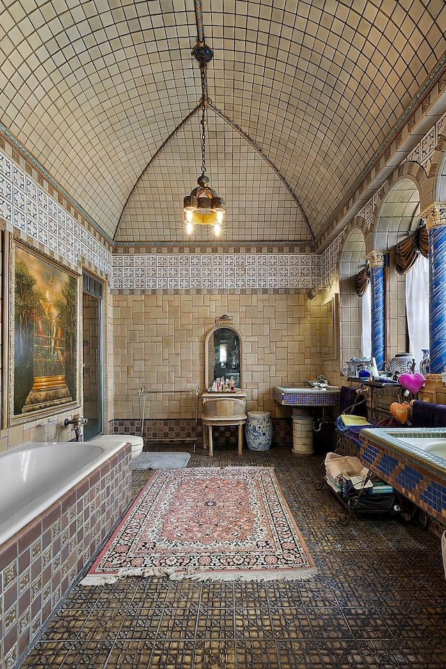 bathroom with tile walls, a relaxing tiled tub, and lofted ceiling