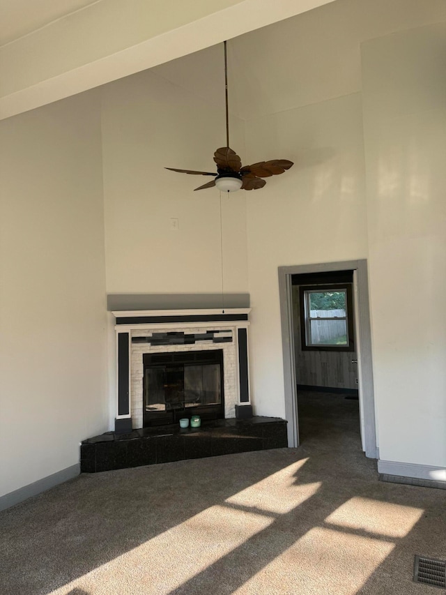 unfurnished living room with carpet, ceiling fan, a fireplace, and a towering ceiling