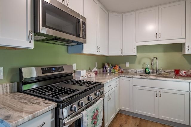 kitchen with appliances with stainless steel finishes, light hardwood / wood-style flooring, white cabinetry, and sink