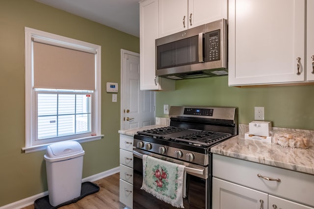 kitchen with white cabinets, light stone counters, light wood-type flooring, and appliances with stainless steel finishes