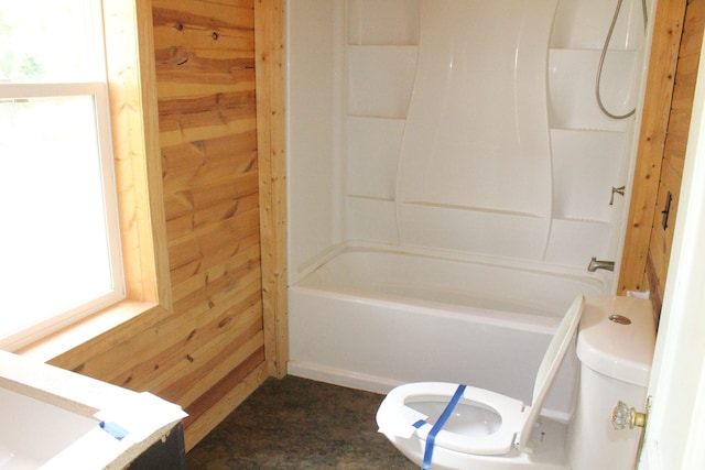 bathroom with wooden walls, shower / bathing tub combination, and toilet