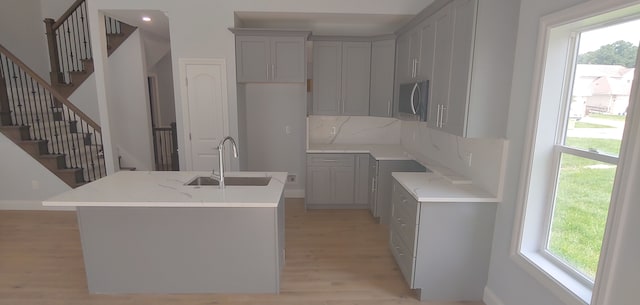 kitchen with sink, light stone counters, backsplash, an island with sink, and light hardwood / wood-style floors