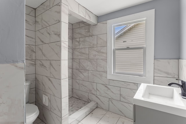 bathroom featuring a tile shower, vanity, toilet, and tile walls