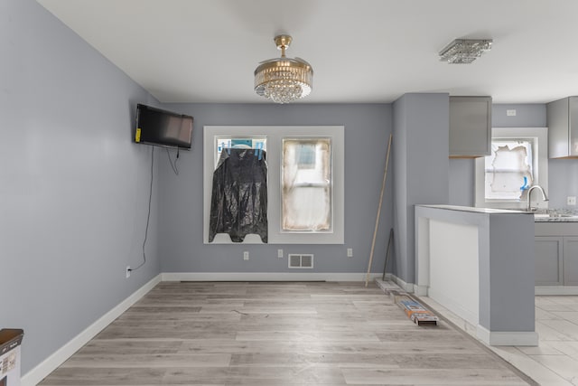 unfurnished dining area with light wood-type flooring, sink, and an inviting chandelier