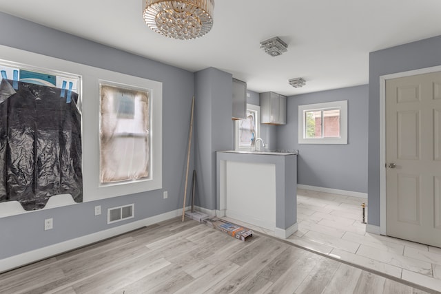 kitchen with gray cabinetry, sink, a chandelier, and light wood-type flooring