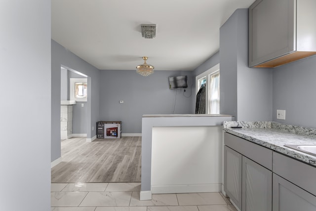 kitchen with gray cabinets, light stone countertops, kitchen peninsula, and light wood-type flooring