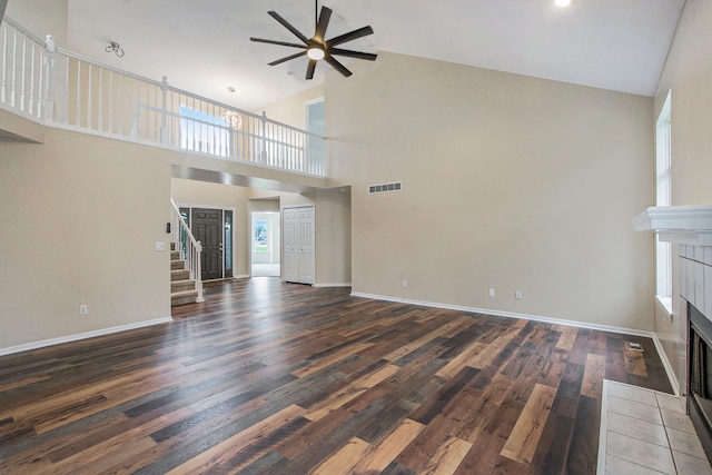 unfurnished living room with high vaulted ceiling, ceiling fan, dark wood-type flooring, and a tiled fireplace