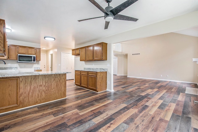 kitchen featuring sink, ceiling fan, light stone counters, dark hardwood / wood-style flooring, and kitchen peninsula