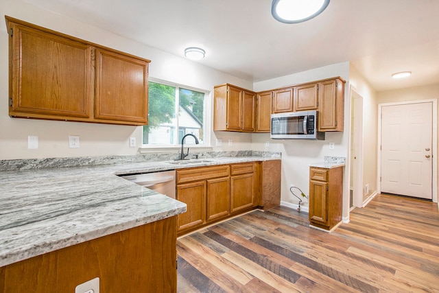 kitchen featuring light stone countertops, light wood-type flooring, stainless steel appliances, and sink